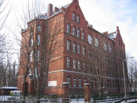 Das Backsteingebäude der Talschule mit Giebeln und hohen Fenstern im Winter, davor kahle Bäume
